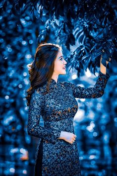 a woman standing under a tree with her hands in the air and looking at something