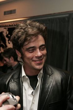 a man in a black leather jacket holding a cell phone and smiling at the camera