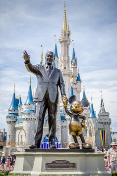 a statue of walt and mickey mouse in front of the castle