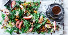 a salad with apples and other vegetables on a wooden table next to a bowl of dressing