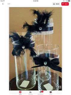 two clear vases with black feathers and crystal beads on them are sitting on a table