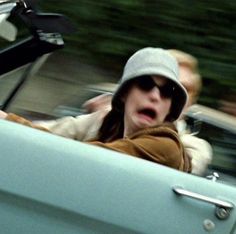 a woman driving in the back seat of a blue car with a surprised look on her face