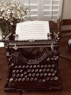 an old fashioned typewriter sitting on top of a wooden table next to a vase with flowers