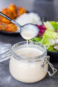 a spoon pouring milk into a jar with salad in the background on a counter top