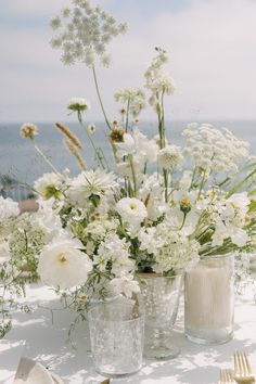 white flowers are in vases on a table with goldware and utensils