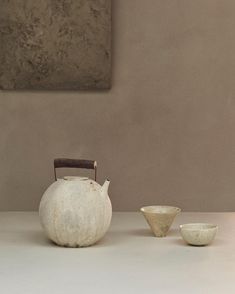 an old teapot and two bowls sit on a table in front of a painting