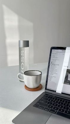 an open laptop computer sitting on top of a white table next to a coffee cup