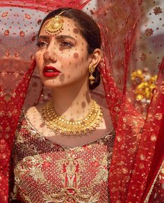 a woman wearing a red and gold bridal outfit with her veil draped over her head