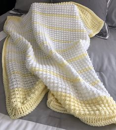 a yellow and white crocheted blanket laying on top of a bed next to pillows