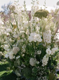 white flowers and greenery are in a vase on the grass near a wooden bench