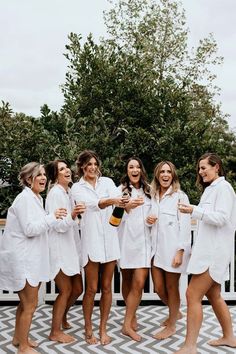 the bridesmaids are all dressed in white robes and holding champagnes while standing together