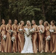 a group of women standing next to each other in front of trees and grass with bouquets