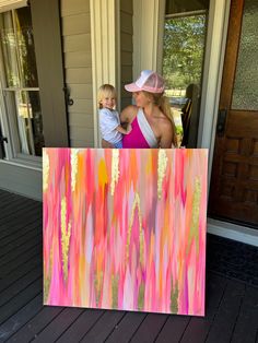 a woman holding a small child in front of a painting on the outside of a house