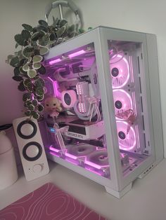 a white computer case sitting on top of a desk next to a plant and speakers