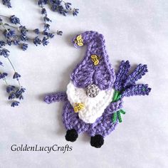 a crocheted purple and white stuffed animal next to lavender flowers on a white surface