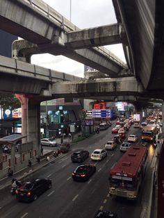 cars and buses are traveling down the busy street in traffic under an overpass on a cloudy day