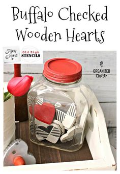 a glass jar filled with wooden hearts sitting on top of a table next to flowers