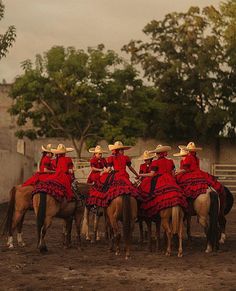 four women in red dresses are riding on horses and one is wearing a cowboy hat