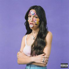 a woman with her arms crossed and painted in sugar skulls on her face, standing against a purple background