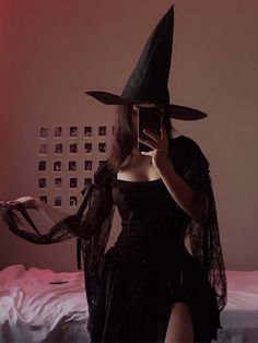 a woman in a witch costume taking a selfie with her cell phone while sitting on a bed