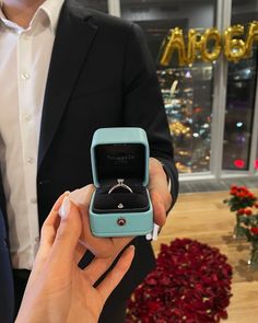 a person holding an open ring box with a diamond in it and wearing a suit