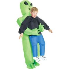 a young boy sitting on top of an inflatable green monster costume with his arm around the head