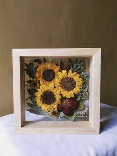 a bouquet of sunflowers in a wooden frame on a white cloth covered table