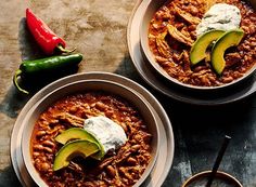 two bowls filled with chili, beans and avocado on top of a table