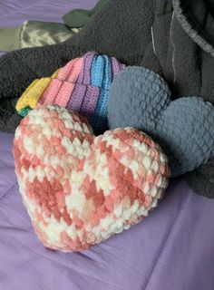 a heart shaped stuffed animal laying on top of a purple blanket next to a black jacket