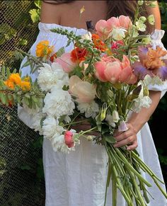 a woman holding a bouquet of flowers in her hands and wearing a white dress with an off the shoulder top