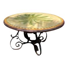 a table with a green leaf design on it's top and wrought iron legs