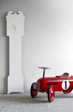 a red toy car sitting in front of a white wall with a clock on it