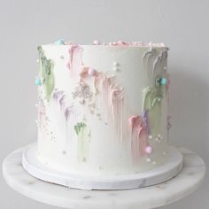 a white cake with pink, green and blue icing sitting on top of a table