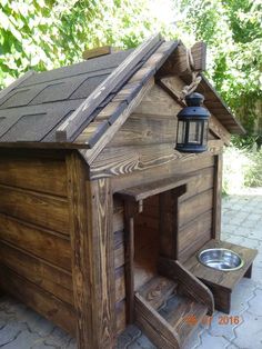 a dog house made out of wood with a water bowl on the outside and a lantern hanging from the roof