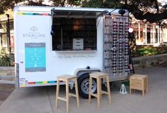 a white food truck parked on the side of a road next to some tables and chairs