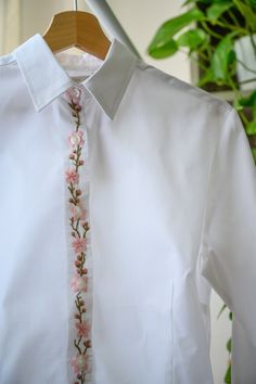 a white dress shirt with pink flowers on the side and a tie hanging from it's chest