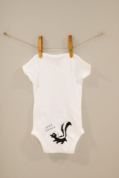 This adorable baby bodysuit makes a perfect outfit for your baby, or gift for any of your favorite  little stinkers in your life  The placement of the design, which is on the babies' bottom, can be adjusted if you wish. The wording "little stinker" can also be changed for additional personalization! 🥰 These custom short-sleeved bodysuits are soft cotton jersey material with overlapping sections at shoulders and snap fasteners at gusset.  This bodysuit is white, and the design is black, unless otherwise discussed via messages. 🤍 Feel free to message us with any questions or requests! 💌 * * * * * * * * * * * * * * * * * * * * * * * * * * * * * * * * * * * * * * *  Care Instructions: * Only non-chlorine bleach when needed * No dry clean * Do not iron on print * Medium iron * Machine wash c Cotton Bodysuit With Cartoon Print And Short Sleeves, Fitted Short Sleeve Bodysuit With Cartoon Print, Fitted Short Sleeve Cotton Bodysuit With Cartoon Print, Funny Cotton Onesie For Babies, Playful Cotton Bodysuit, Fitted Short Sleeve Cartoon Print Bodysuit, Playful Cotton Onesie For First Birthday, White Fitted Short Sleeve Bodysuit With Graphic Print, Cute Unisex Cotton Onesie