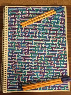 two pencils sitting on top of a spiral notebook with an abstract pattern and blue, green, purple, and yellow colors