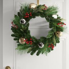 a christmas wreath hanging on the front door with ornaments around it and red berries, pine cones, and silver bells