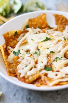 a white bowl filled with nachos covered in cheese and sauce next to tortilla chips