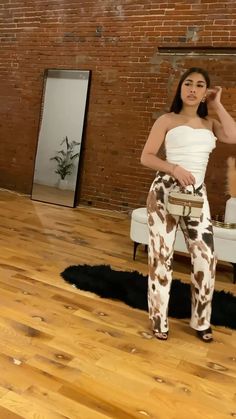 a woman standing on top of a hard wood floor next to a brick wall and wearing cow print pants