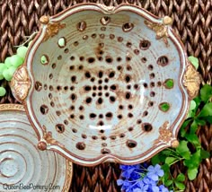 a decorative bowl sitting on top of a table next to blue and green flowers in front of a wicker basket