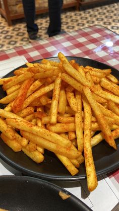 french fries on a black plate with a red and white checkered tablecloth in the background