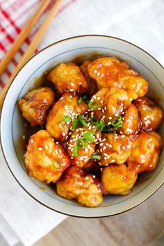 a bowl filled with chicken and sesame seeds on top of a table next to chopsticks