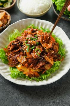 a white plate topped with meat and lettuce next to bowls filled with rice