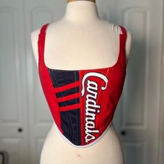 Over-bust corset with flexible boning and silk ribbon closure.  Made from a Cardinals jersey with white cotton pinstripe in back. Fits a small  - US 2-6 (sizing is pretty flexible due to the lace up closure) Mannequin's measurements - Waist: 27" Bust: 37" Let me know if you have any questions. Red Fitted Top With Boned Bodice, Sleeveless Lace-up Back Corset, Fitted Overbust Top With Corset Back, Sporty Fitted Top With Straps, Stretch Corset With Tank Straps And Corset Back, Fitted Cotton Top With Corset Back, Stretch Corset With Corset Back And Tank Straps, Fitted Underbust Top With Corset Back, Fitted Red Tops With Straps