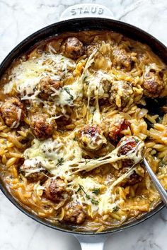 a skillet filled with pasta and meatballs covered in grated parmesan cheese