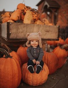 a little boy sitting on top of a pile of pumpkins wearing a bear hat