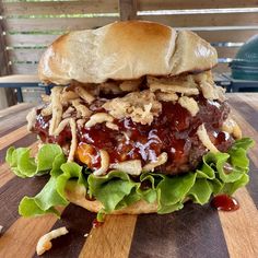 a large hamburger with meat, lettuce and sauce on it sitting on top of a wooden table