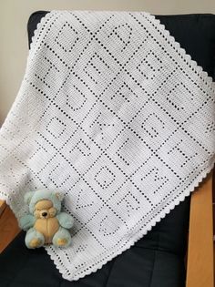 a teddy bear sitting on top of a chair next to a crocheted blanket